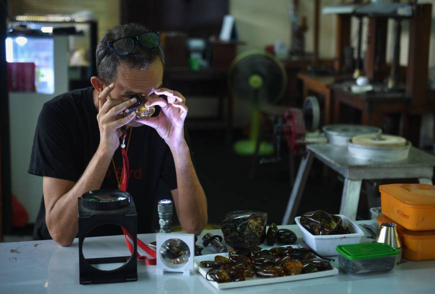 Akbar Khan, a 52-year-old self-described 'extreme fossil in amber hunter,' inspects a piece of honey-colored fossilized tree sap from Kachin state in Myanmar at his street stall in Bangkok on May 31. | AFP-JIJI
